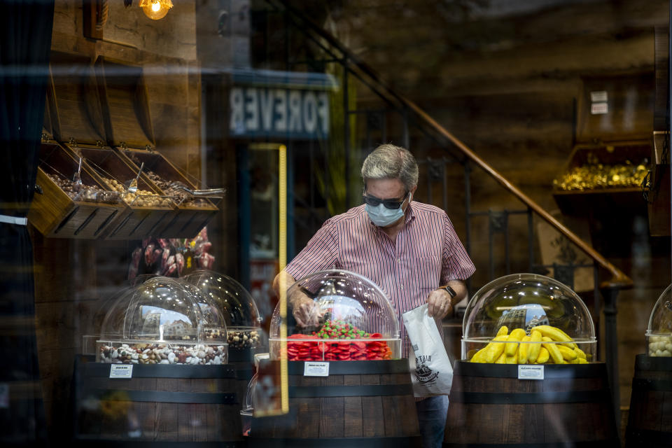 A man wearing a face mask to prevent the spread of coronavirus buys sweets in downtown Madrid, Spain, Wednesday, Sept. 16, 2020. The Spanish capital will introduce selective lockdowns in urban areas where the coronavirus is spreading faster, regional health authorities announced on Tuesday. (AP Photo/Manu Fernandez)