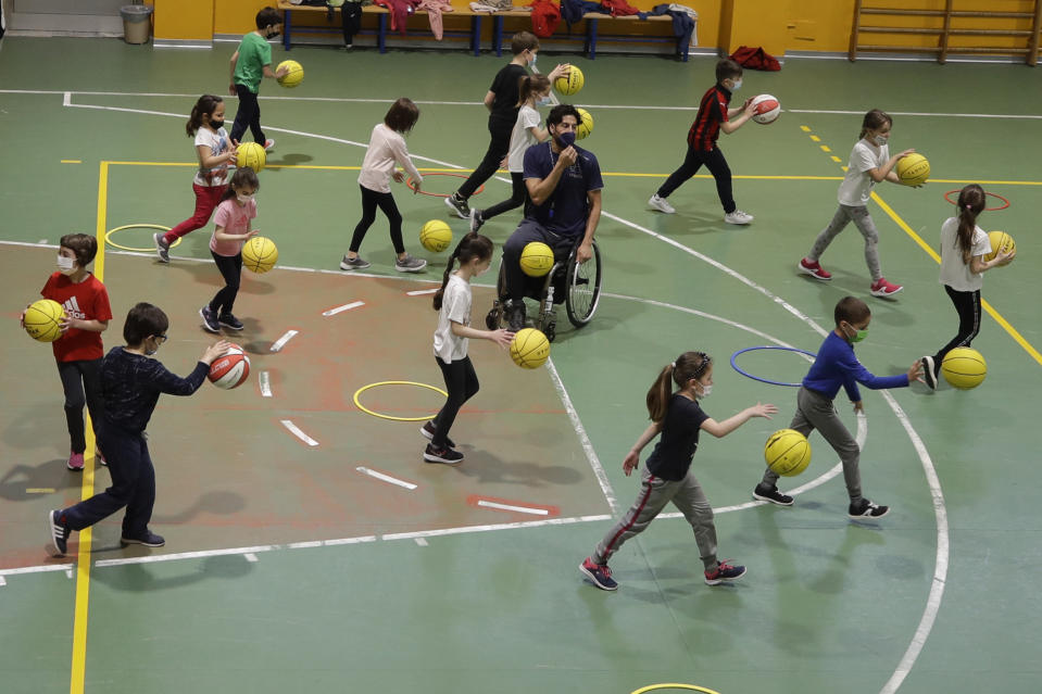 Adolfo Damian Berdun, of Argentina, a professional player and captain of the Argentine basketball Paralympic team, teaches children basketball at a primary school in Verano Brianza, outskirt of Milan, Italy, Tuesday, May 11, 2021. Four second-grade classes in the Milan suburb of Verano Brianza have been learning to play basketball this spring from a real pro. They also getting a lesson in diversity. Their basketball coach for the last month has been Adolfo Damian Berdun, an Argentinian-Italian wheelchair basketball champion. Berdun, 39, lost his left leg in a traffic accident at ag 13 in his native Buenos Aires, and he has visited many schools over the years to discuss how he has lived with his disability. (AP Photo/Luca Bruno)