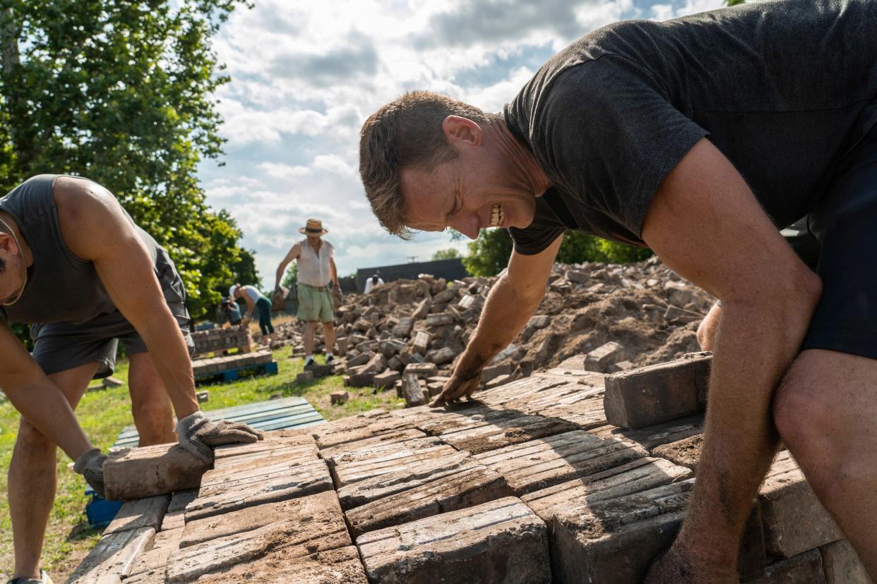 Jeff Cowin, right, of Detroit, works on stacking handmade Nelsonville block pavers onto a pallet to use for repairing Virginia Park Street at a lot along East Vernor Highway in Detroit on Thursday, July 7, 2022.