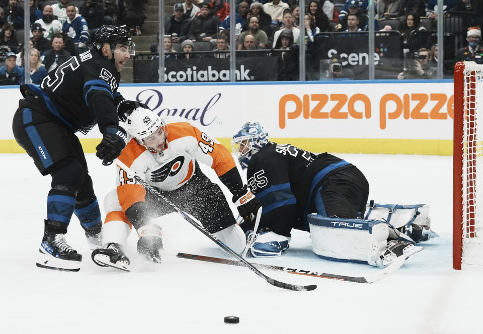 Philadelphia Flyers left wing Noah Cates (49) is checked by Toronto Maple Leafs defenseman Mark Giordano (55) as Maple Leafs goaltender Ilya Samsonov (35) looks on during the third period of an NHL hockey game, Thursday, Dec. 22, 2022 in Toronto. (Chris Young/The Canadian Press via AP)