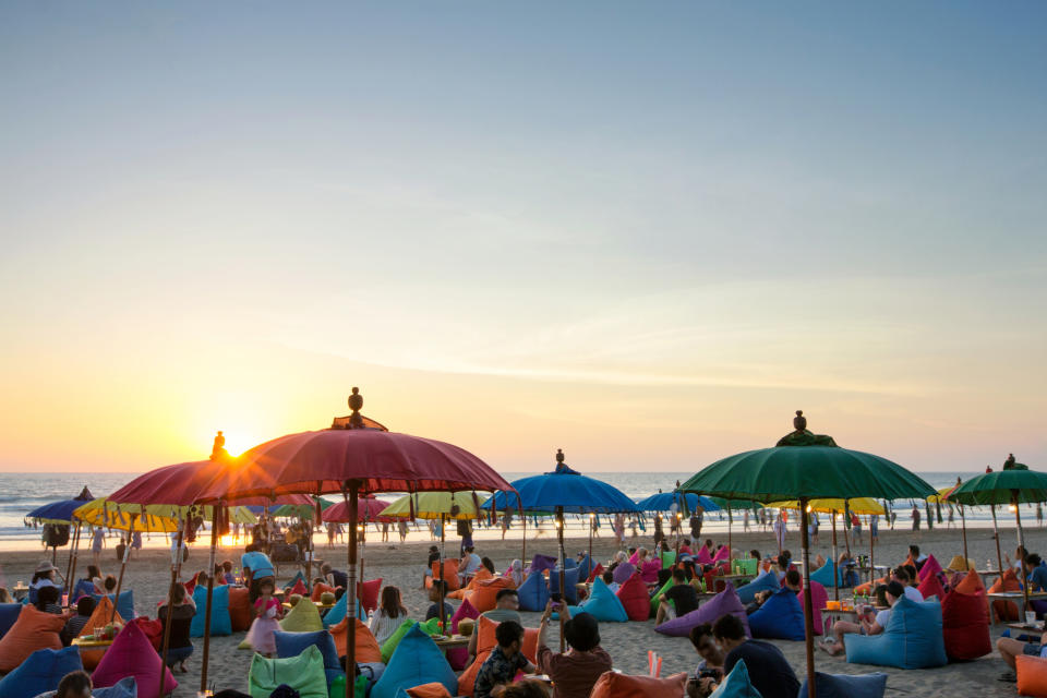 Beach scene with people on bean bags under umbrellas at sunset