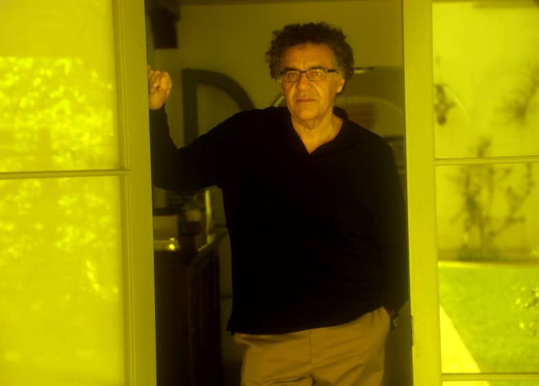Rodrigo Garcia, looking serious, stands between a set of glass doors that reflect yellow light