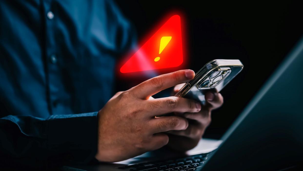  Man holding a mobile phone with warning notification and spam message icon. 