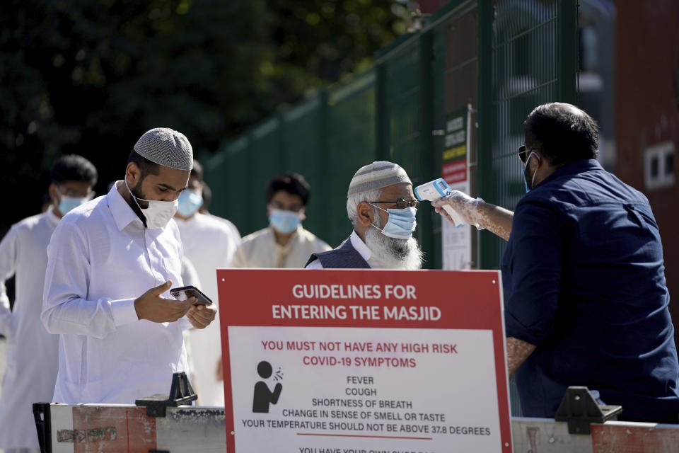 A man wearing a face mask has his temperature checked to try stop the spread of coronavirus, before being allowed to go into Manchester Central Mosque, in Manchester, northern England, as Muslims worldwide mark the start of the Eid al-Adha holiday, Friday, July 31, 2020. The British government on Thursday night announced new rules on gatherings in some parts of Northern England, including Manchester, that people there should not mix with other households in private homes or gardens in response to an increase trend in the number of cases of coronavirus cases per 100,000 people. (AP Photo/Jon Super)