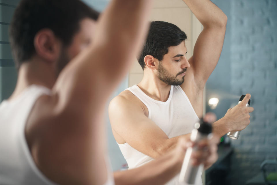 The reflection in the mirror of a man spraying his underarm