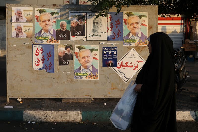 A woman walks near posters of presidential candidates Masoud Pezeshkian and Saeed Jalili displayed in Tehran