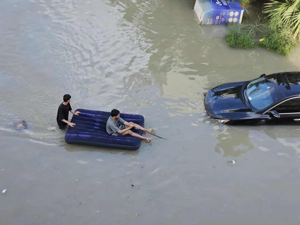 Zwei Männer nutzen eine Luftmatratze, um sich über Wasser zu halten, als ein Wolkenbruch in Dubai schwere Überschwemmungen verursacht. (Anadolu via Getty Images)
