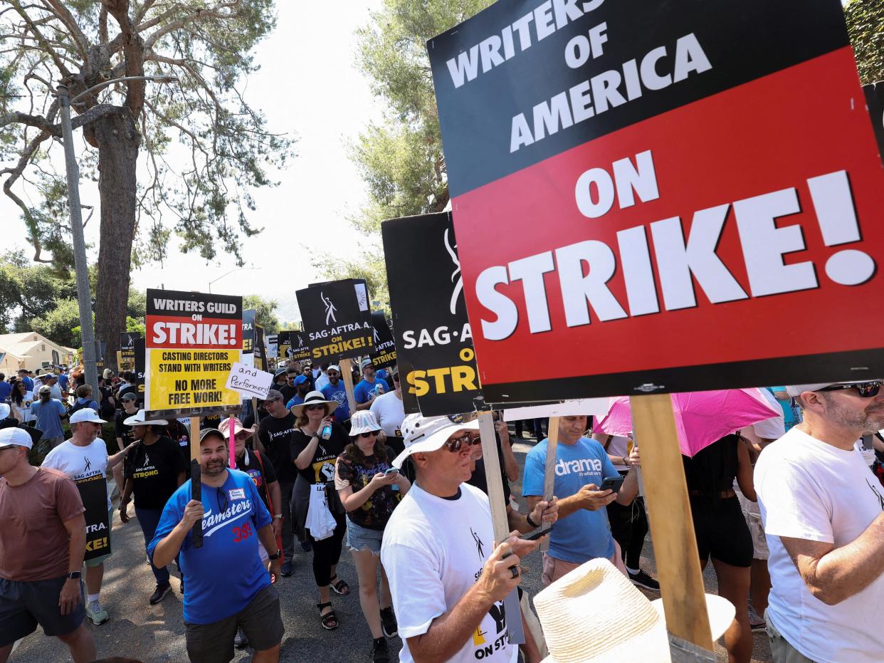 A group of people holding signs related to the SAG-AFTRA and Writers Guild of America strike.