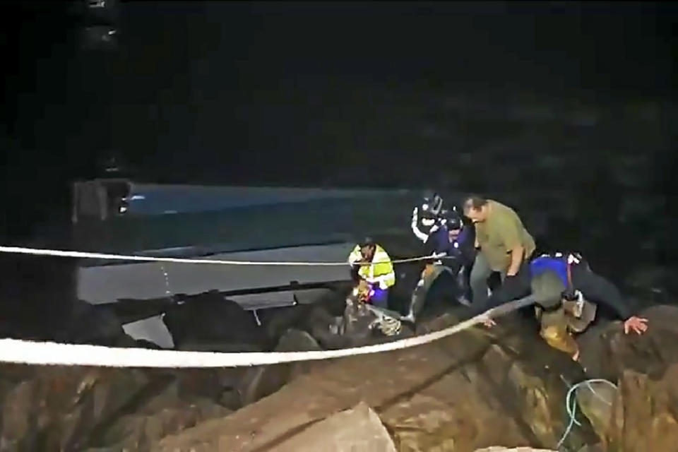 This photo from video provided by Rob Gensorek of Basin Tackle Charleston shows firefighters rescuing the crew from a capsized crab boat in the harbor at Coos Bay, Ore., late Tuesday evening, Jan. 14, 2020. Three men were in good condition early Wednesday after being cut from inside the hull of the capsized boat. The 38-foot (11-meter) Pacific Miner was flipped upside-down by large waves late Tuesday and then got caught on rocks in a jetty in Coos Bay as the tide went out. A U.S. Coast Guard helicopter on a routine training mission spotted the vessel and launched a rescue, the agency said in a news release. (Rob Gensorek of Basin Tackle Charleston via AP)