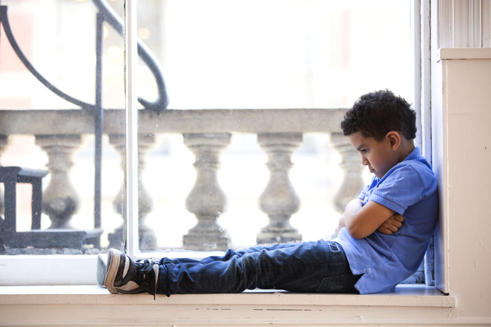 Child sitting by a window, arms crossed, looking outside. Appears contemplative or waiting