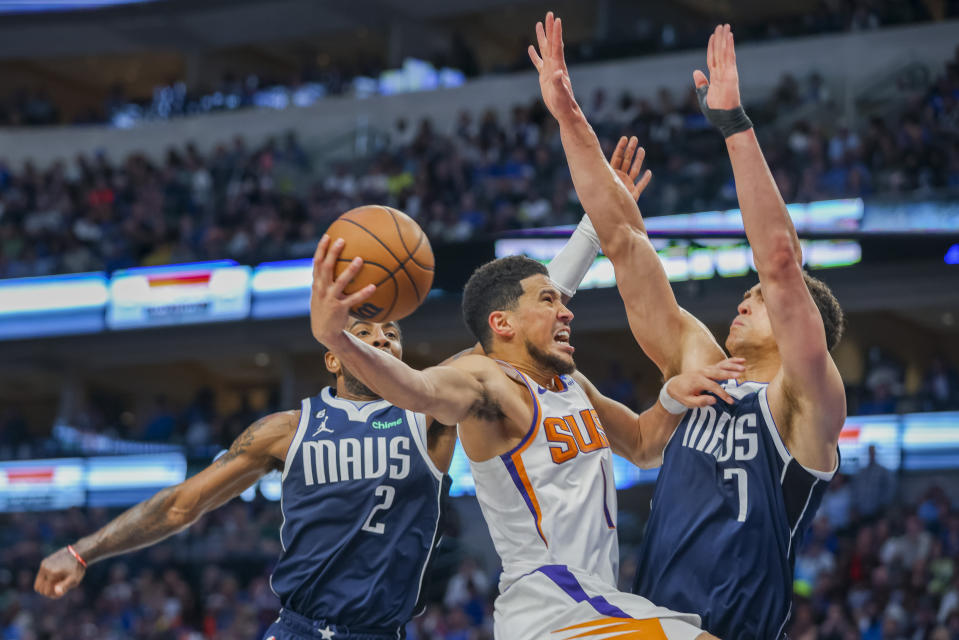 Phoenix Suns guard Devin Booker, center, drives to the basket as Dallas Mavericks players Kyrie Irving, left, and Dwight Powell, right, defend during the second half of an NBA basketball game, Sunday, March 5, 2023, in Dallas. (AP Photo/Gareth Patterson)