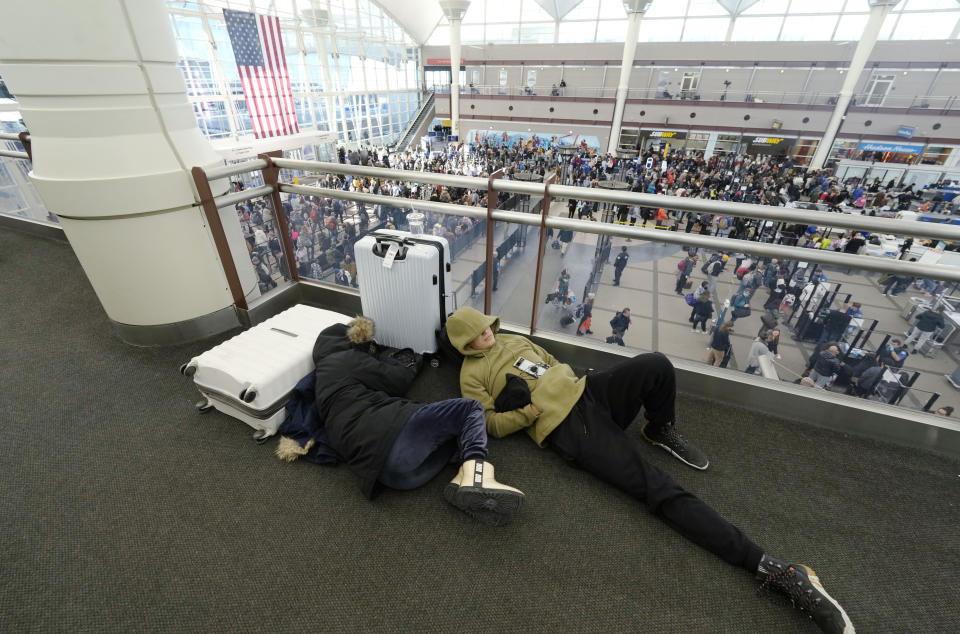 A pair of travelers sleep while fellow travelers queue up below to pass through the south security checkpoint in Denver International Airport after a winter storm swept over the country packing snow combined with Arctic cold, which created chaos for people trying to reach their destinations before the Christmas holiday, Friday, Dec. 23, 2022, in Denver. Forecasters predict that warmer weather will be on tap for the week ahead. (AP Photo/David Zalubowski)