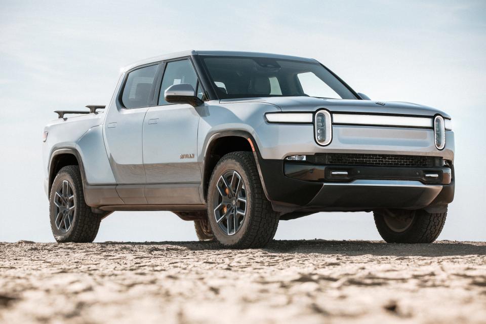 A silver Rivian R1T on a rocky surface against a gray sky.