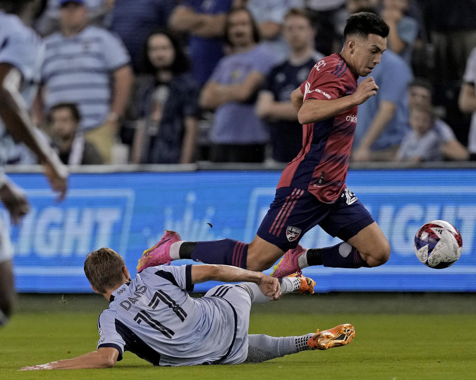 FC Dallas forward Alan Velasco trips over Sporting Kansas City midfielder Jake Davis (17) as he chases the ball during the first half of an MLS soccer match Wednesday, May 31, 2023, in Kansas City, Kan. (AP Photo/Charlie Riedel)