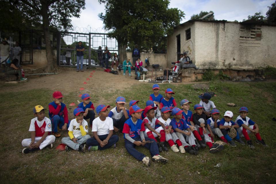 In this Aug. 12, 2019 photo, young baseball players sit on a knoll as they wait for instruction from their coach at Las Brisas de Petare Sports Center in Caracas, Venezuela. In the country that has been a quarry for stars like Miguel Cabrera and Felix Hernandez, new generations must endure not only the difficulties generated by the worst economic crisis in recent history but also the logistical obstacles. (AP Photo/Ariana Cubillos)