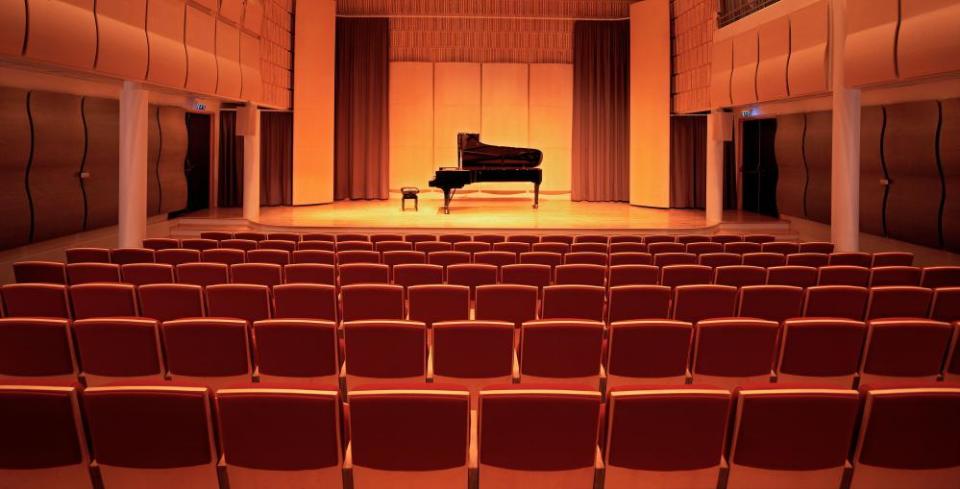 A piano on stage inside an empty concert hall