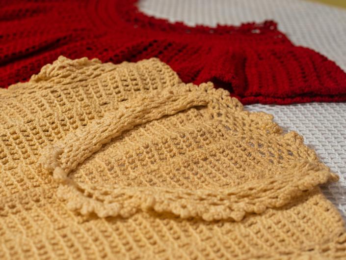 Two crochet tops, one yellow one red, on white blanket