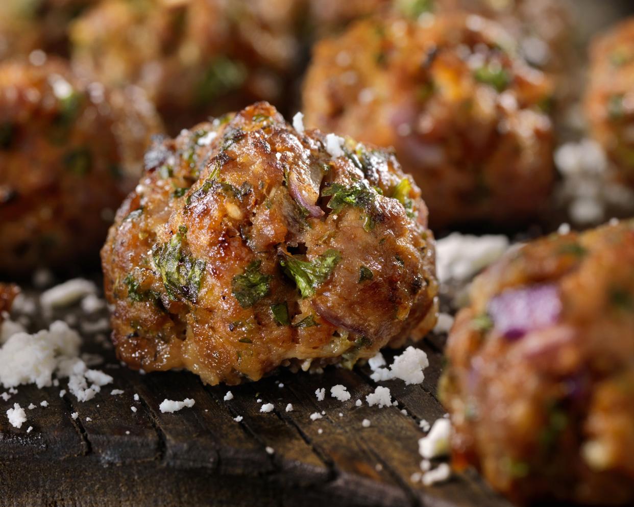 Closeup of a meatball surrounded by blurred meatballs on a wooden stab with bits of parmesan cheese