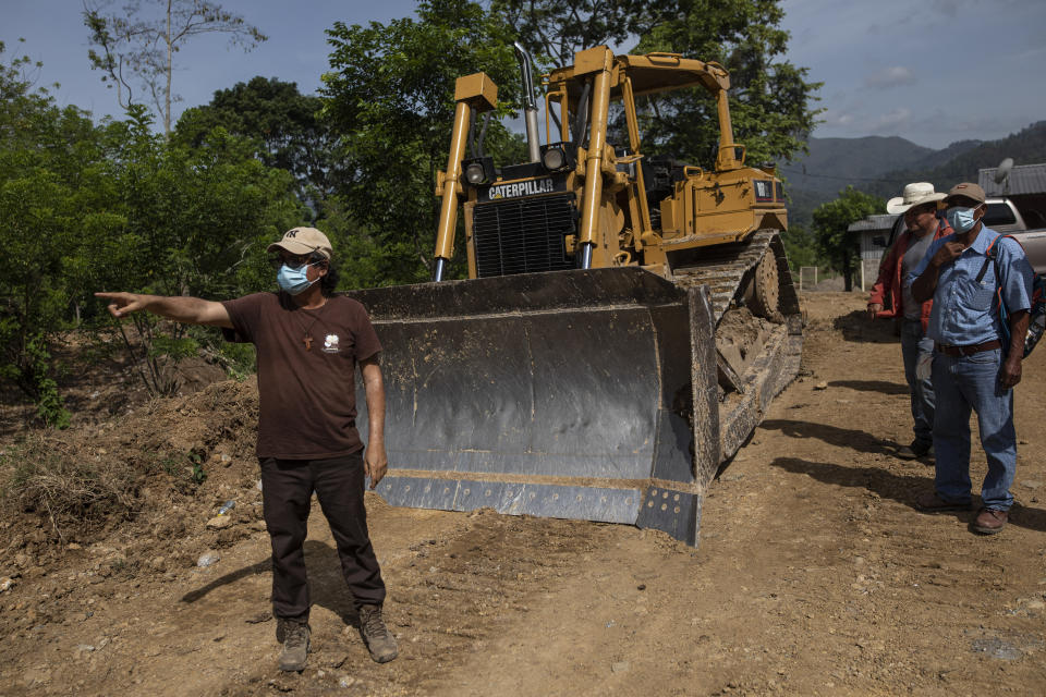 Friar Leopoldo Serrano shows bulldozer operators which direction he would like them to pave a road for a new community being constructed for the residents of La Reina, whose homes were devastated by a mudslide triggered by Hurricanes Eta and Iota, in Mission San Francisco de Asis, Honduras, Tuesday, June 22, 2021. Twenty-five years ago, the powerful local cartel run by Arnulfo Valle bought the 70 acres adjacent to the mission where Father Serrano hopes to put those displaced from La Reina. (AP Photo/Rodrigo Abd)