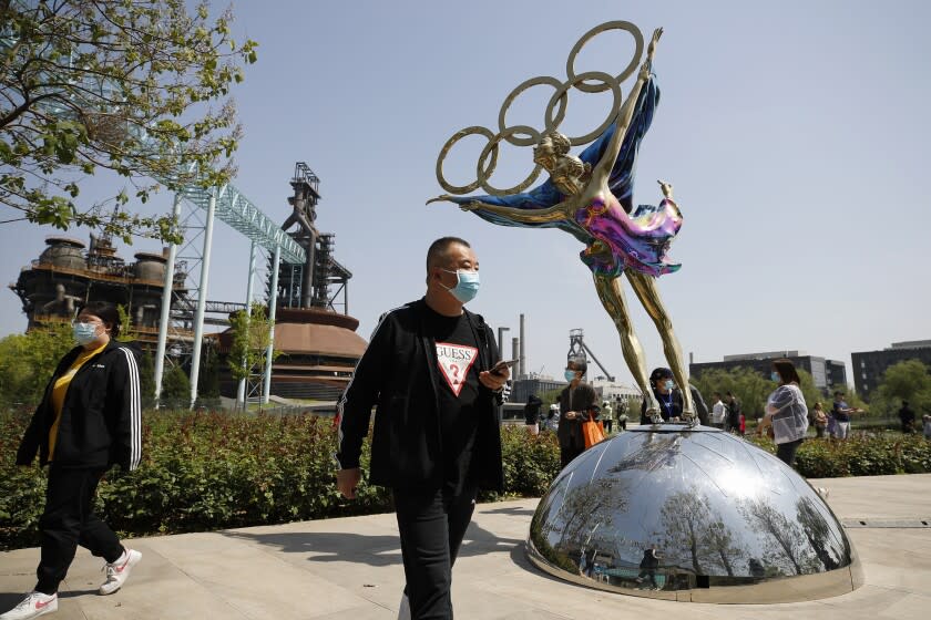 FILE - Visitors wearing face masks to help curb the spread of the coronavirus walk by a statue featuring Winter Olympics figure skating on display at the Shougang Park in Beijing, Sunday, May 2, 2021. Making an Olympic team is hard enough. This winter, those who earn their spots on the U.S. squad will find it takes even more work to get to Beijing. (AP Photo/Andy Wong, File)