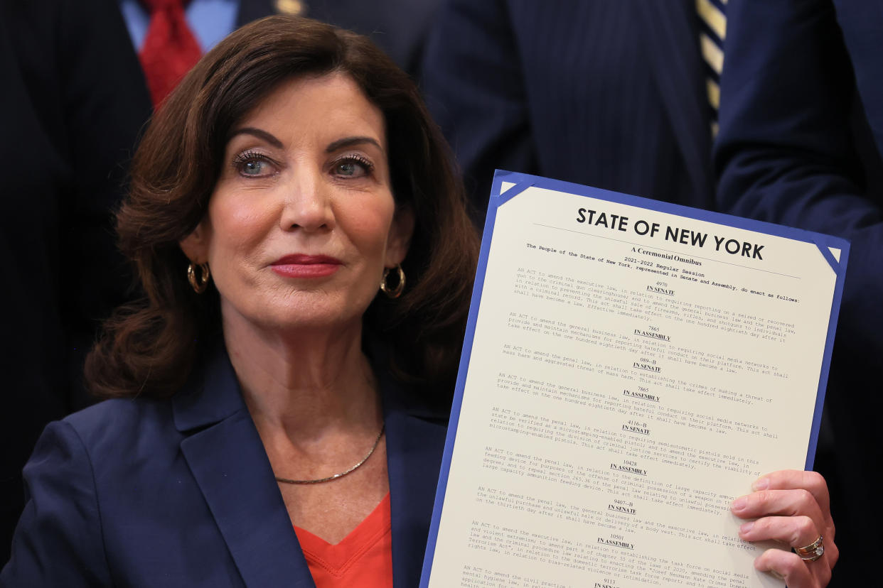 Gov. Kathy Hochul, looking defiant, holds up signed legislation under the heading State of New York.