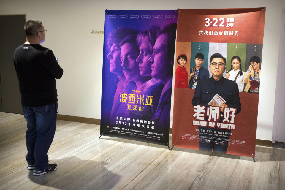 A customer looks at a movie poster for the film "Bohemian Rhapsody" at a movie theater in Beijing, Wednesday, March 27, 2019. Moviegoers in China say the version of the "Bohemian Rhapsody" shown in Chinese theaters erases mentions of Freddie Mercury's sexuality. The biopic on the lead singer of the British rock band Queen omitted a same-sex kiss and lacked scenes in which Mercury reveals he's not straight and has AIDS. (AP Photo/Mark Schiefelbein)