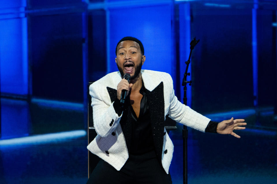 John Legend singt leidenschaftlich auf der Bühne und trägt einen weißen Blazer mit schwarzen Details, ein schwarzes Hemd und eine schwarze Hose