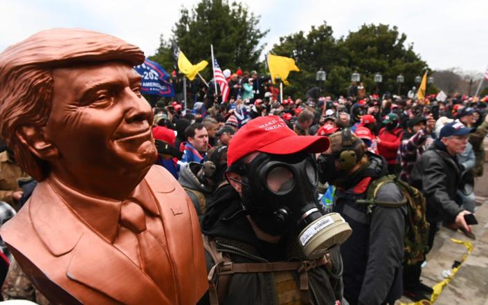 A supporter of US President Donald Trump wears a gas mask and holds a bust of him after he and hundreds of others stormed stormed the Capitol building - Roberto Schmidt/AFP