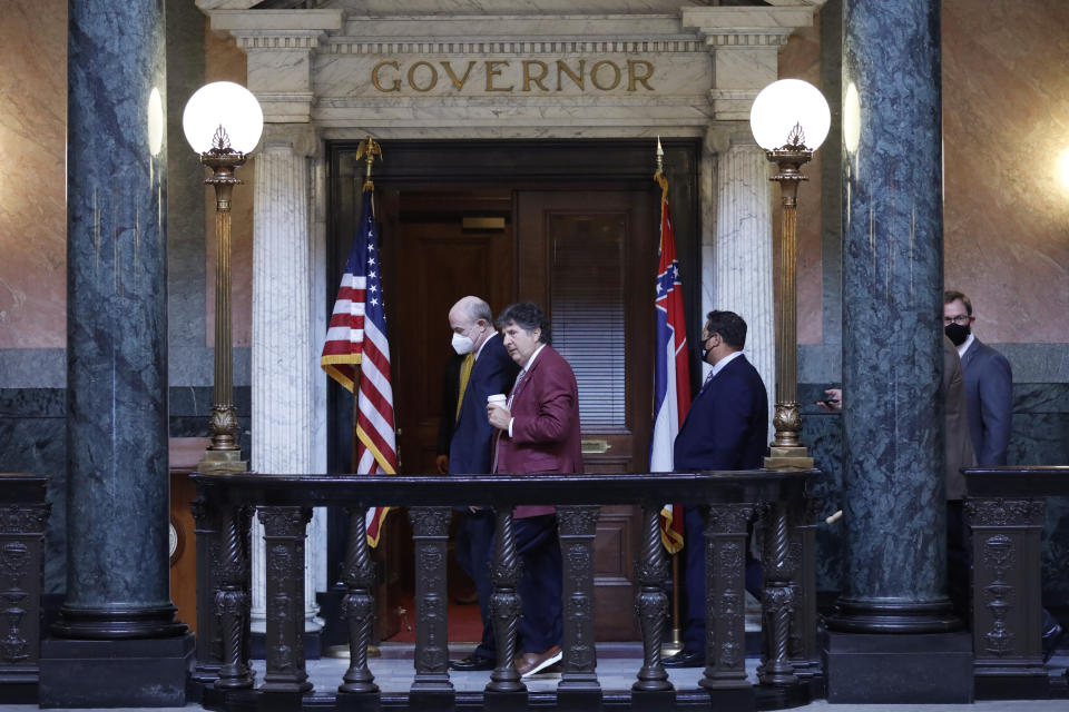 Mississippi State basketball coach Ben Howland, left, and football coach Mike Leach, center, walk past the Mississippi state flag, at right, on their way to the governor's office at the Capitol in Jackson, Miss., Thursday, June 25, 2020. Head sports coaches from Mississippi State and the state's other public universities met with Lt. Gov. Delbert Hosemann, House Speaker Philip Gunn and other lawmakers to call for the removal of the Civil War-era Confederate battle flag from the design of the Mississippi state flag. (AP Photo/Rogelio V. Solis)