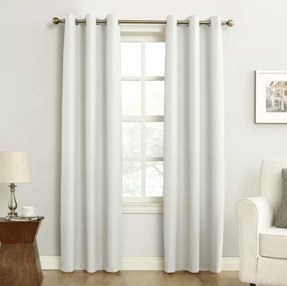 A pair of plain white curtains hang on a rod in front of a window in a styled room