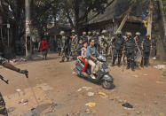 Indian paramilitary soldiers stand guard, as people ride past on a scooter in New Delhi, India, Wednesday, Feb. 26, 2020. At least 20 people were killed in three days of clashes in New Delhi, with the death toll expected to rise as hospitals were overflowed with dozens of injured people, authorities said Wednesday. The clashes between Hindu mobs and Muslims protesting a contentious new citizenship law that fast-tracks naturalization for foreign-born religious minorities of all major faiths in South Asia except Islam escalated Tuesday. (AP Photo/Manish Swarup)