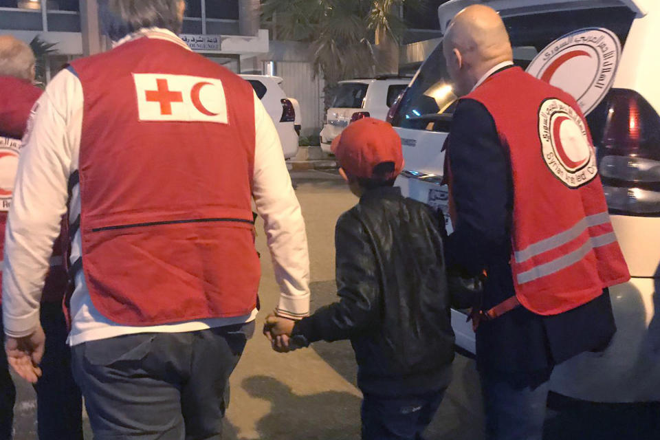 In this photo taken Wednesday, Nov. 6, 2019, Alvin, an 11-year-old Albanian boy who was taken to Syria by his mother when she joined the Islamic State group, is accompanied to Damascus airport by Red Cross and Red Crescent officials, after he was freed from a crowded detention camp. The boy, who found himself with no family in the al-Hol camp run by Kurdish forces in northeastern Syria after his mother and siblings died amid fighting, is heading home, to Italy, where his father lives. (International Federation of Red Cross and Red Crescent photo via AP)