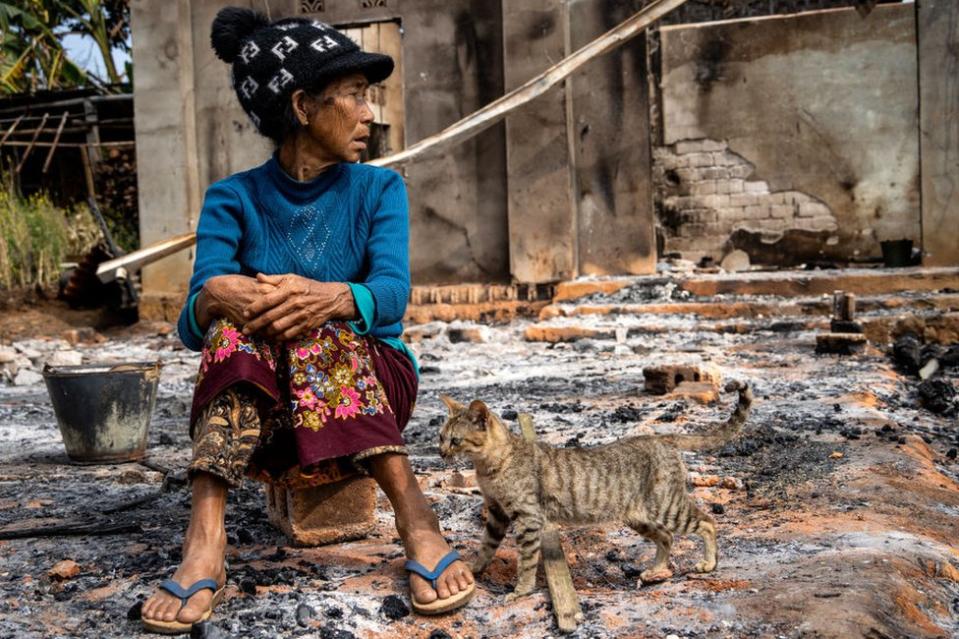 This photo taken on February 4, 2024 shows a woman sitting next to a cat in front of her house damaged following fighting between Myanmar's Military and the Kachin Independence Army (KIA) in Nam Hpat Kar, Kutkai township in Myanmar's northern Shan State.