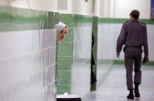 PHOTO: FILE - An Iranian inmate peers from behind a wall as a guard walks by at the female section of the infamous Evin jail, north of Tehran, 13 June 2006. (Atta Kenare/AFP via Getty Images, FILE)