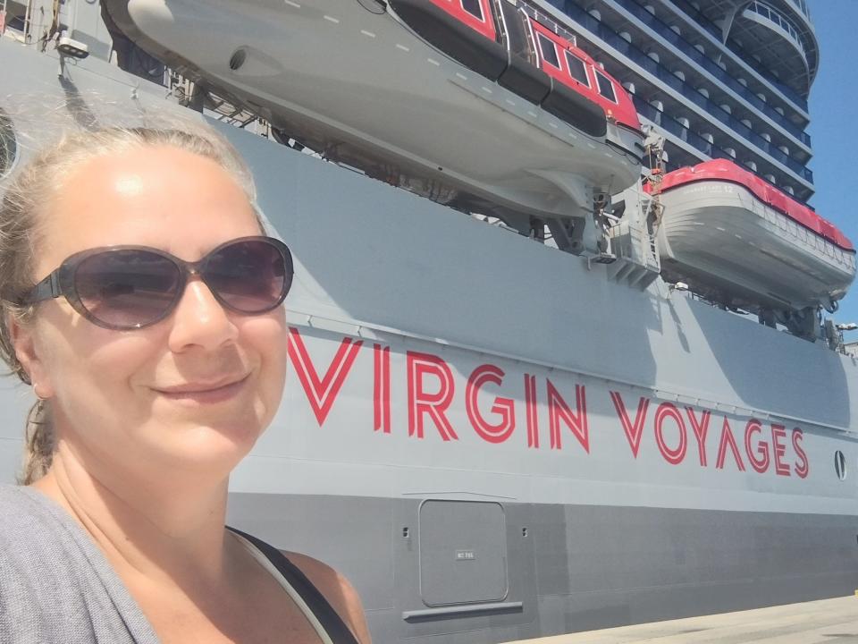 woman smiling in front of virgin voyages scarlet lady ship