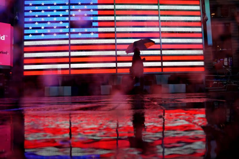 Pedestrian walks in the rain past a U.S. flag displayed in Times Square in New York City