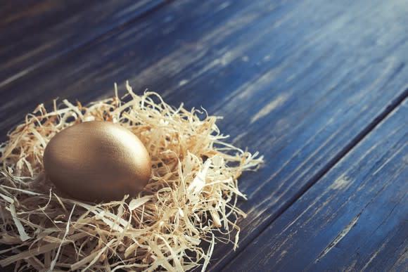 A golden egg in a nest that's resting on a piece of wood.