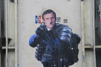 A graffiti shows French President Emmanuel Macron dressed like a riot police officer and aiming at protesters during a demonstration Thursday, Dec. 19, 2019 in Paris. Traffic improved slightly on French trains Thursday as nationwide strikes over the government's retirement reform entered a 15th day and small signs of progress emerged in negotiations with unions. (AP Photo/Michel Euler)