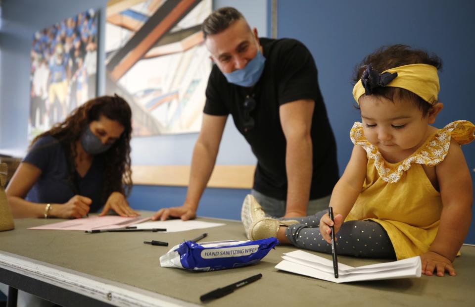 A young girl uses pen and paper as a woman site and a man stands