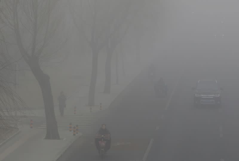 FILE PHOTO: People drive and ride amid the smog in Beijing