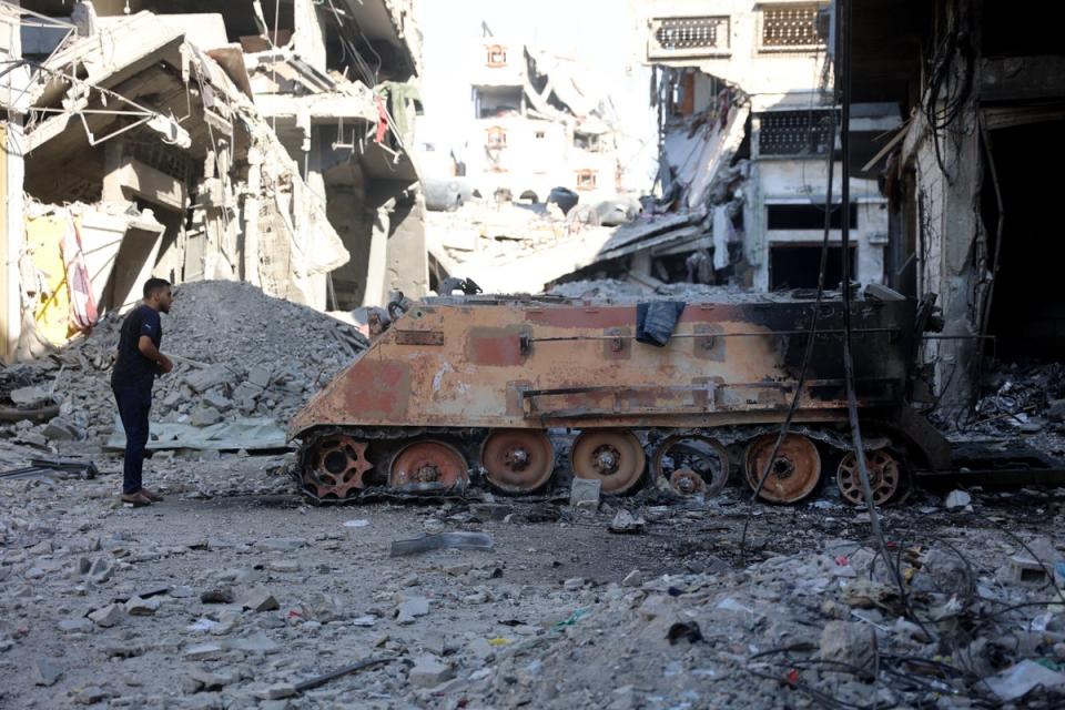 A Palestinian man looks at a destroyed Israeli military vehicle seen near the destroyed buildings and rubble (AFP via Getty Images)