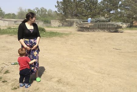 A woman with a boy looks at a tank as it drives through the settlement Khutor Chkalova on its way to the Russian military training ground 'Kuzminsky' near the Russian-Ukrainian border in the Rostov region, Russia, May 26, 2015. REUTERS/Maria Tsvetkova