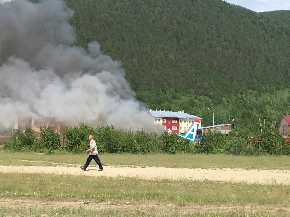 A man walks past a burning An-24 plane a fire after a crash during a landing in Nizhneangarsk, Republic of Buryatia, Russia, Thursday, June 27, 2019. According to the Russian Emergency Ministry, the two dead were members of the cabin crew. Forty-six passengers have been rescued, the ministry said. (AP Photo/Vladimir Dozmorov)
