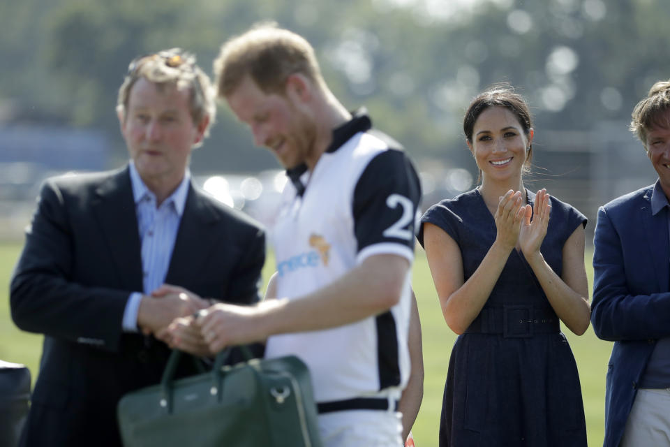 FILE - In this Thursday, July 26, 2018 file photo, Meghan, Duchess of Sussex applauds Prince Harry, foreground, during the presentation ceremony for the Sentebale ISPS Handa Polo Cup at the Royal County of Berkshire Polo Club in Windsor, England. Prince Harry and his wife, Meghan, are fulfilling their last royal commitment Monday March 9, 2020 when they appear at the annual Commonwealth Service at Westminster Abbey. It is the last time they will be seen at work with the entire Windsor clan before they fly off into self-imposed exile in North America. (AP Photo/Matt Dunham, file)