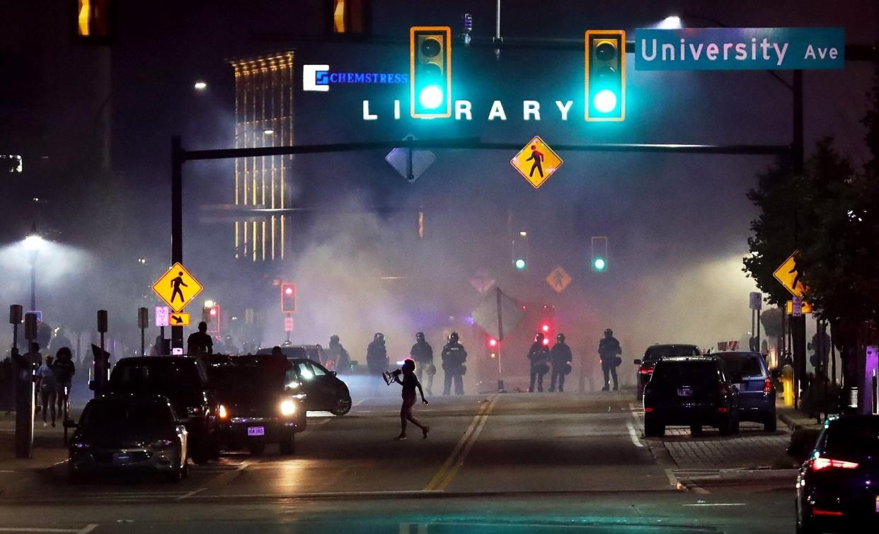 A protester runs through tear gas as officers in riot gear progress down Main Street near University Avenue during protests July 3, 2022, in response to the shooting death of Jayland Walker.