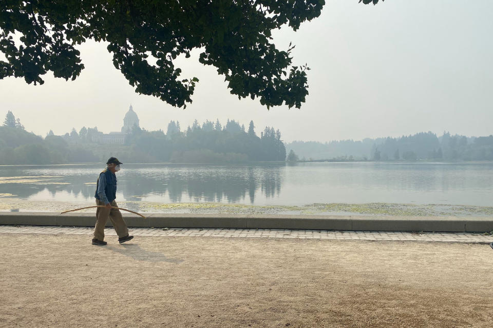 A man wearing a mask walks by the lake outside of the Washington State Capitol in Olympia, Wash., Friday, Sept. 11, 2020. Olympia is among the places facing unhealthy air quality due to wildfires in the Pacific Northwest. (AP Photo/Rachel La Corte)
