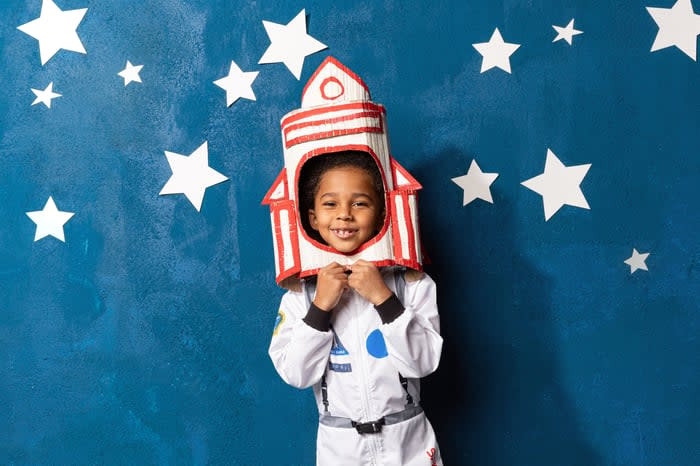 A child in a spacesuit with a handcrafted rocket on their head.