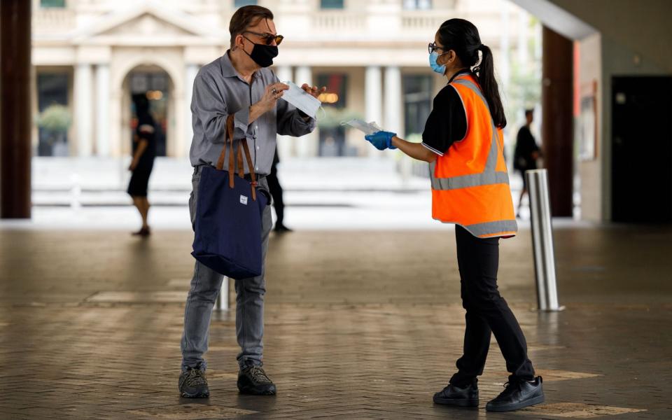 A commuter is handed a face mask by a worker in Sydney, New South Wales, Australia, 03 January 2021. Mandatory mask restrictions are in place for many venues across greater Sydney as New South Wales works to contain COVID-19 outbreaks while avoiding harsh lockdown measures. Coronavirus pandemic in New South Wales, Australia,  - Shutterstock