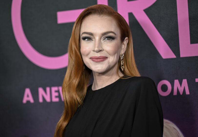 Lindsay Lohan wears a black dress as she smiles while posing for pictures at a red carpet event.