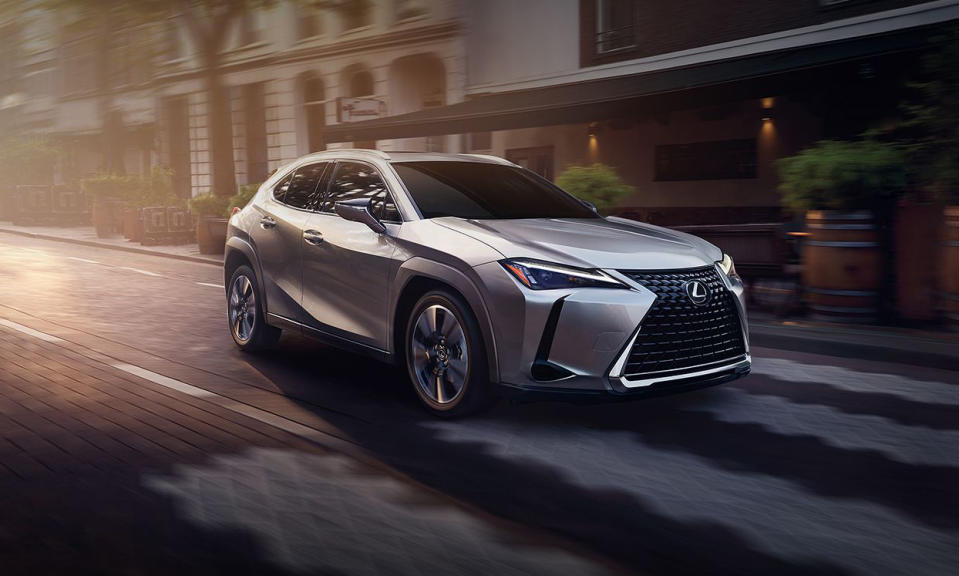 Marketing photo of the Lexus UX hybrid vehicle. The silver model drives down a city street with dramatic lighting.